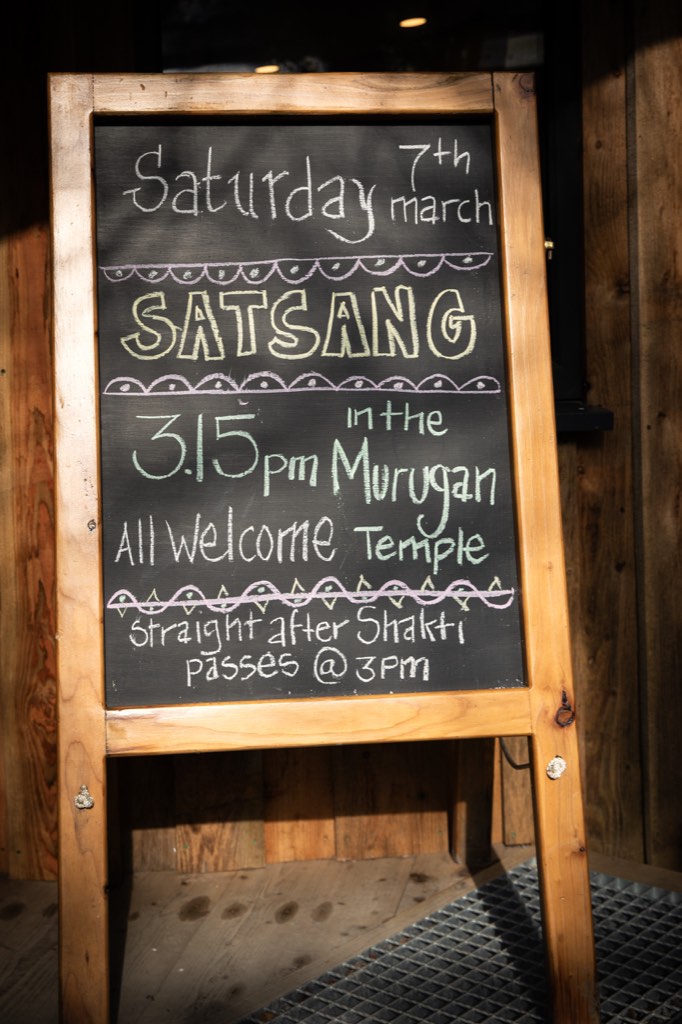 A chalkboard sign on an easel outside the temple, written in coloured chalk: Saturday 7th March, Satsang, 3.15pm in the Murugan Temple, all welcome, straight after Shakti passes at 3pm.